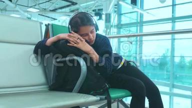 戴着耳机的少女睡在机场等待飞机起飞<strong>登机</strong>口的长椅上
